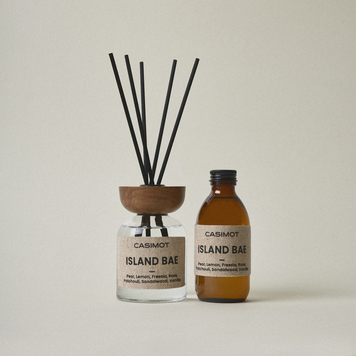 CASIMOT Island Bae reed diffuser with black reeds and wooden lid beside a matching amber refill bottle.