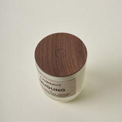 A single jar candle with a dark brown wooden lid and a beige textured label, photographed on a plain light beige background. The label reads 'CASIMOT' and 'MUGUNG'.