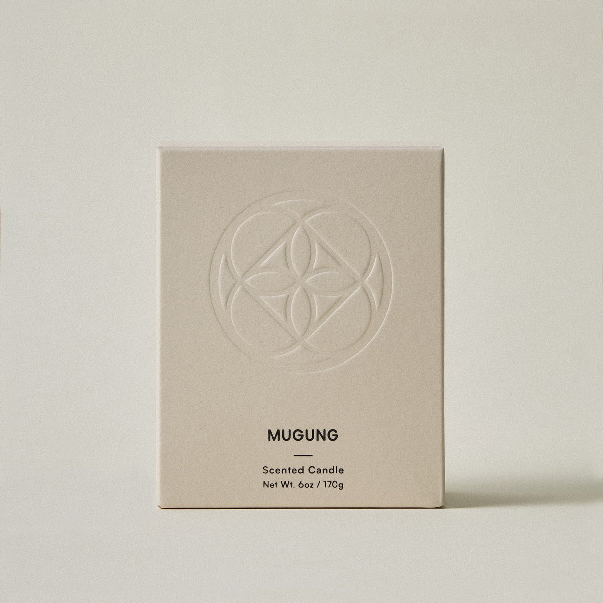 A minimalist beige cardboard box for a Mugung scented candle, featuring an embossed circular geometric logo and black text, set against a matching light beige background.