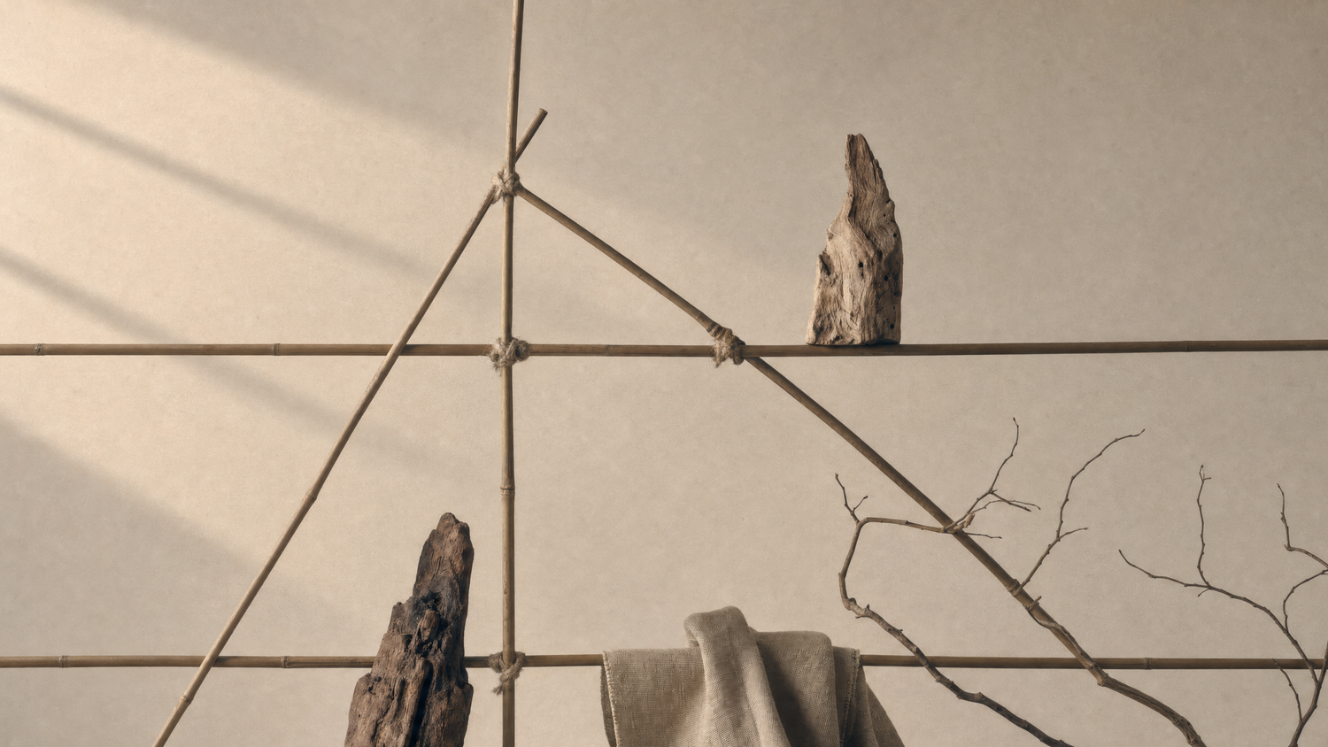 Minimalist beige wall and floor backdrop with a geometric arrangement of thin brown branches and sticks, two rough natural wood pieces, and a draped beige fabric cloth.